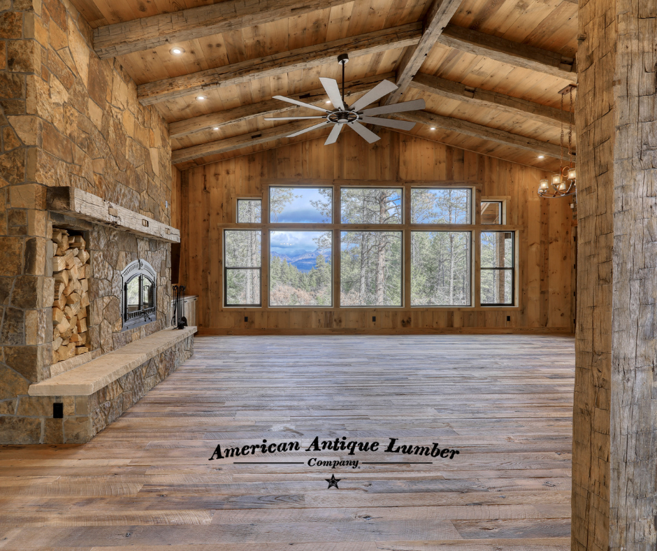 Great room with stone fireplace on left, wall of windows in front and a ceiling fan above. 