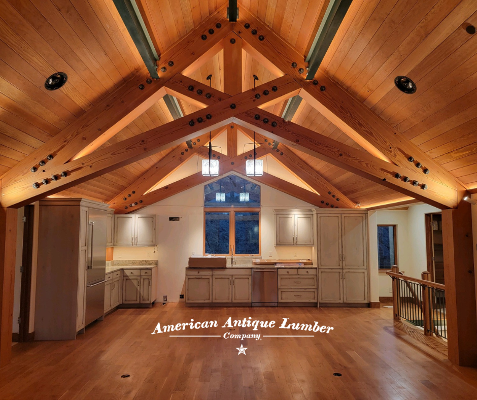 Wood ceiling liner with reclaimed softwood beams, white kitchen cabinets and a window over the sink. 