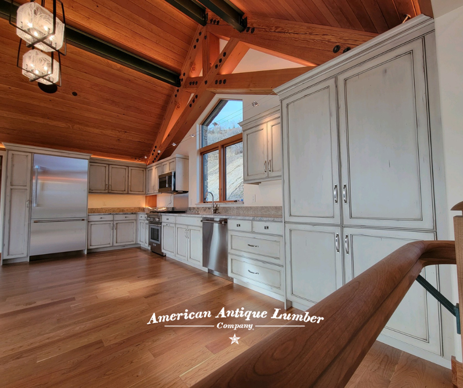White kitchen cabinets with stainless steel appliances, backsplash lighting, and wood floors, beams and ceiling liner. 