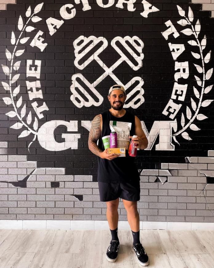A Man is Standing in Front of a Brick Wall Holding Health Products and Supplements — The Factory Gym in Taree, NSW