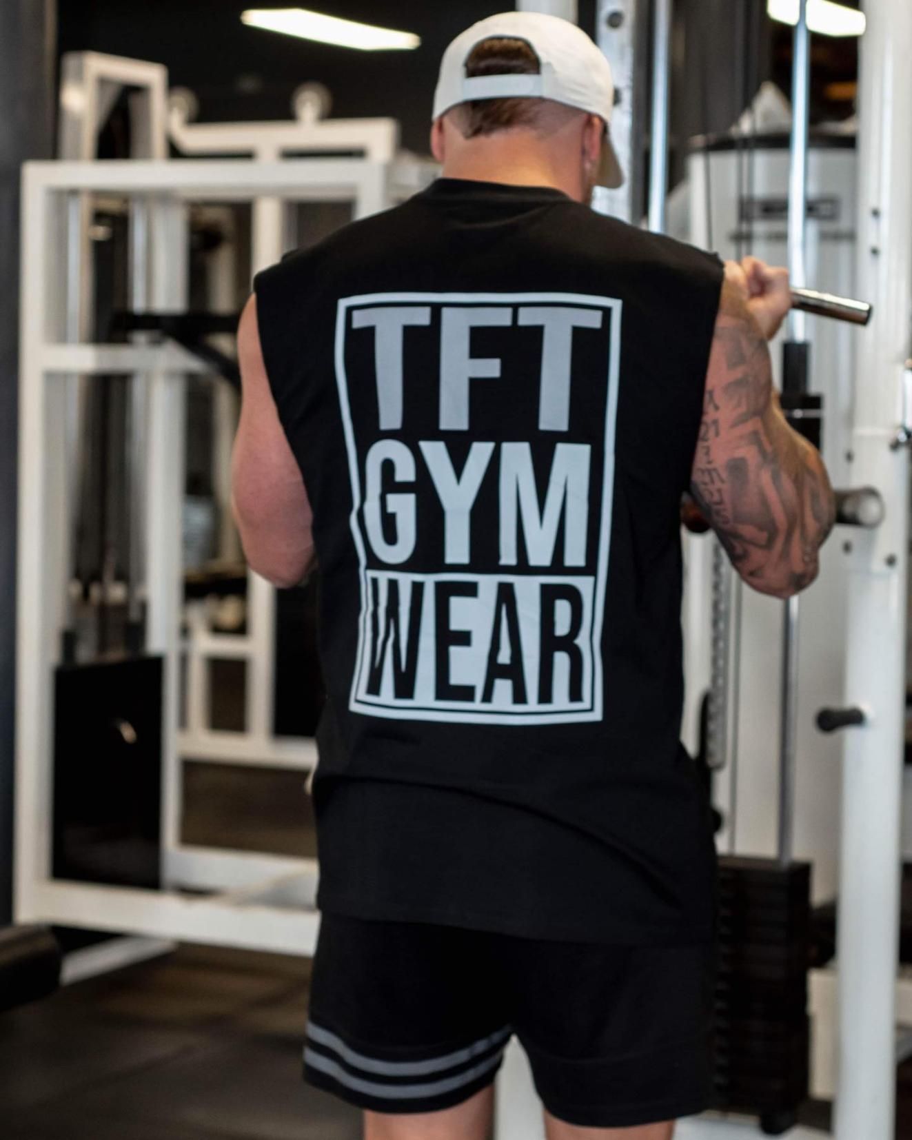 A Man is Squatting on a Machine in a Gym Wearing a TFT Gym Wear Tank  Top — The Factory Gym in Taree, NSW