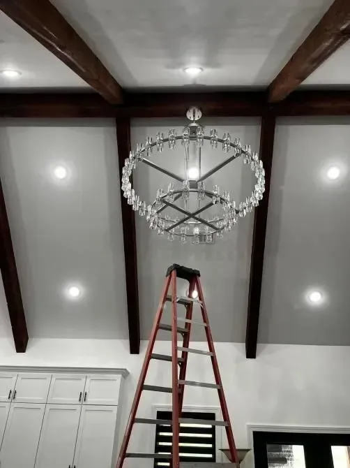 A ladder is sitting under a chandelier in a room.
