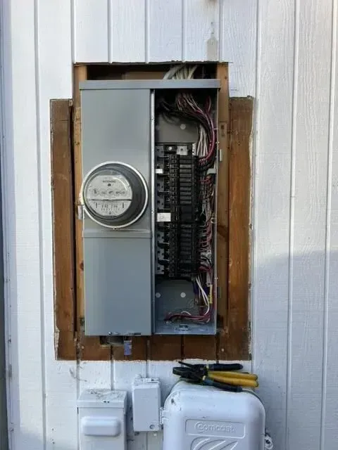 A electrical box is hanging on the side of a building.