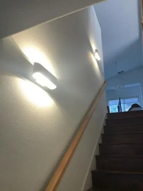 A staircase with a wooden railing and a light on the wall