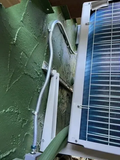 A white air conditioner is mounted to a green wall.