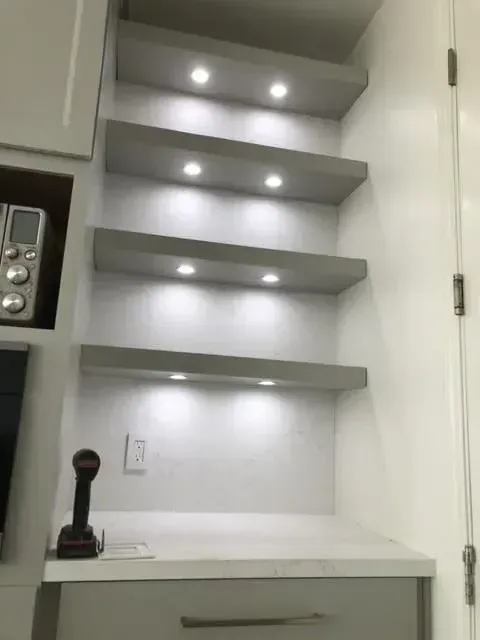 A kitchen with white cabinets and shelves with lights on them.