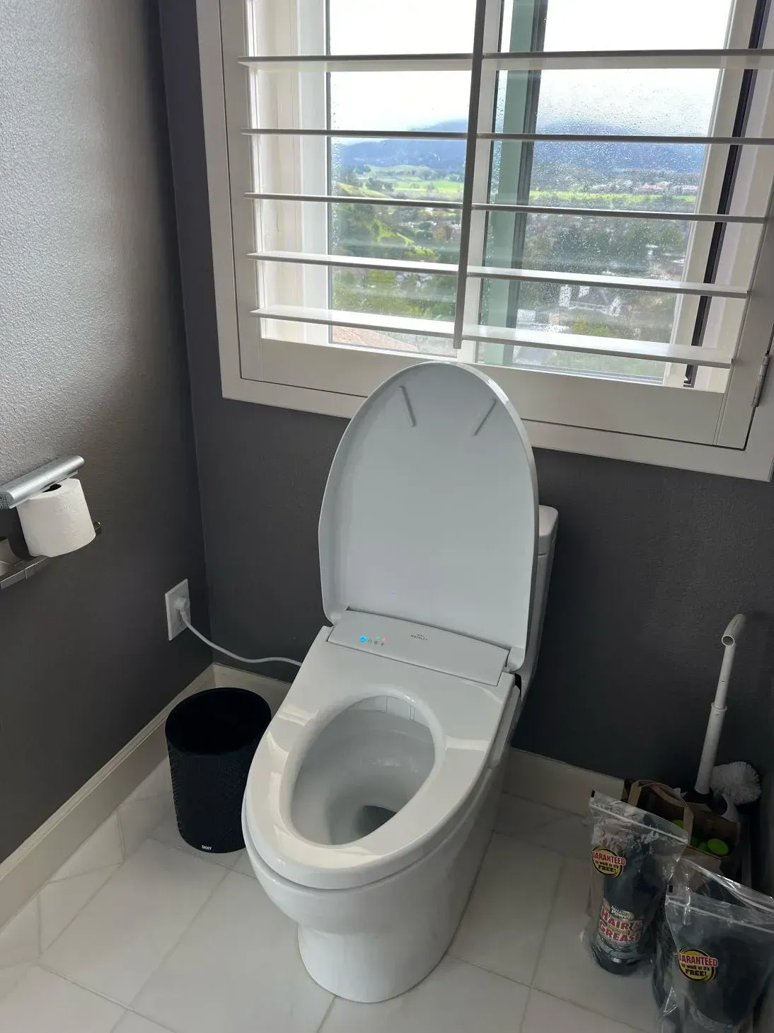 A toilet is sitting in a bathroom next to a window.