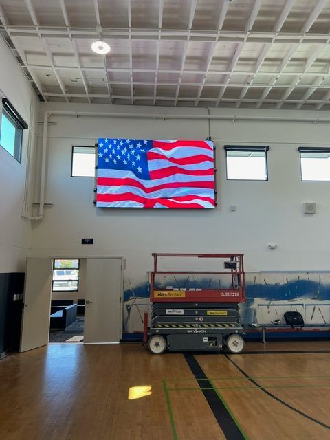 A large american flag is hanging from the ceiling of a gym