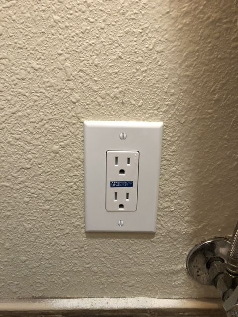 A white electrical outlet on a white wall next to a sink.