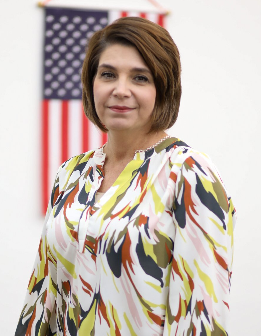 A woman in a colorful shirt is standing in front of an american flag.