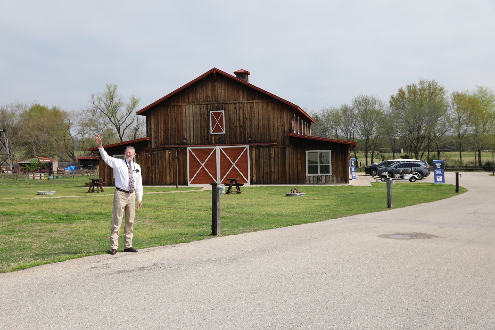 A man is standing in front of a barn with his hand in the air.