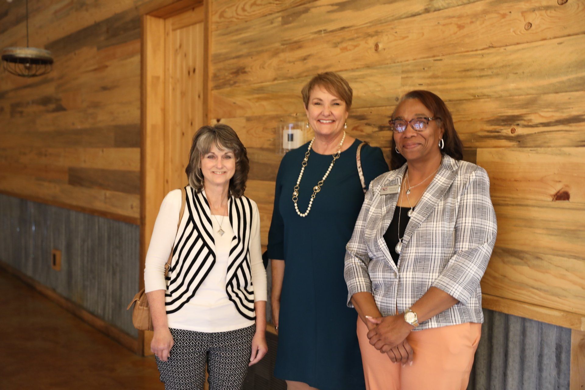 Three women are standing next to each other in front of a wooden wall.