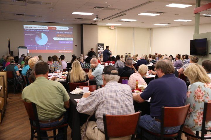 A large group of people are sitting at tables in a room watching a presentation.