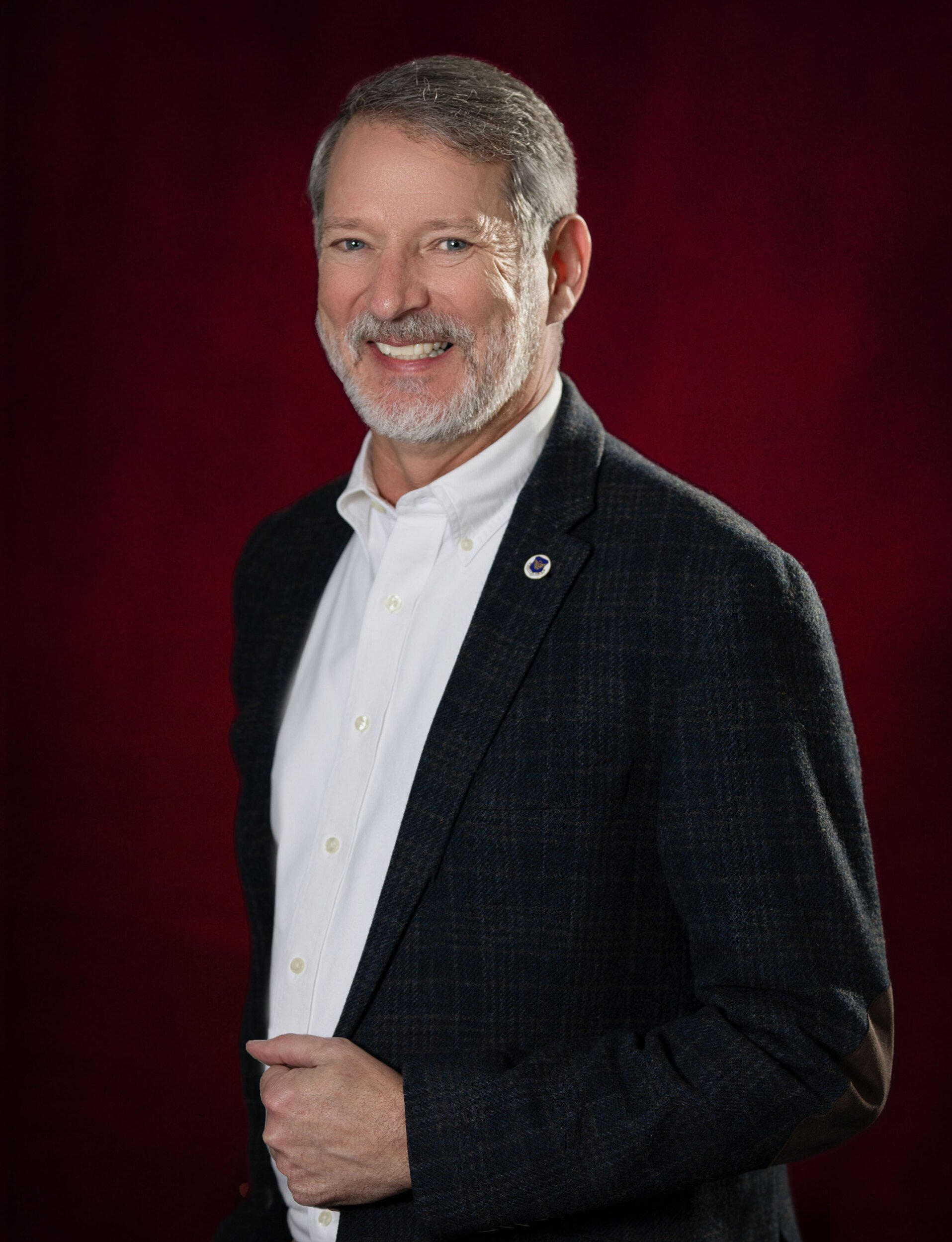 A man in a suit and white shirt is standing in front of a red background.