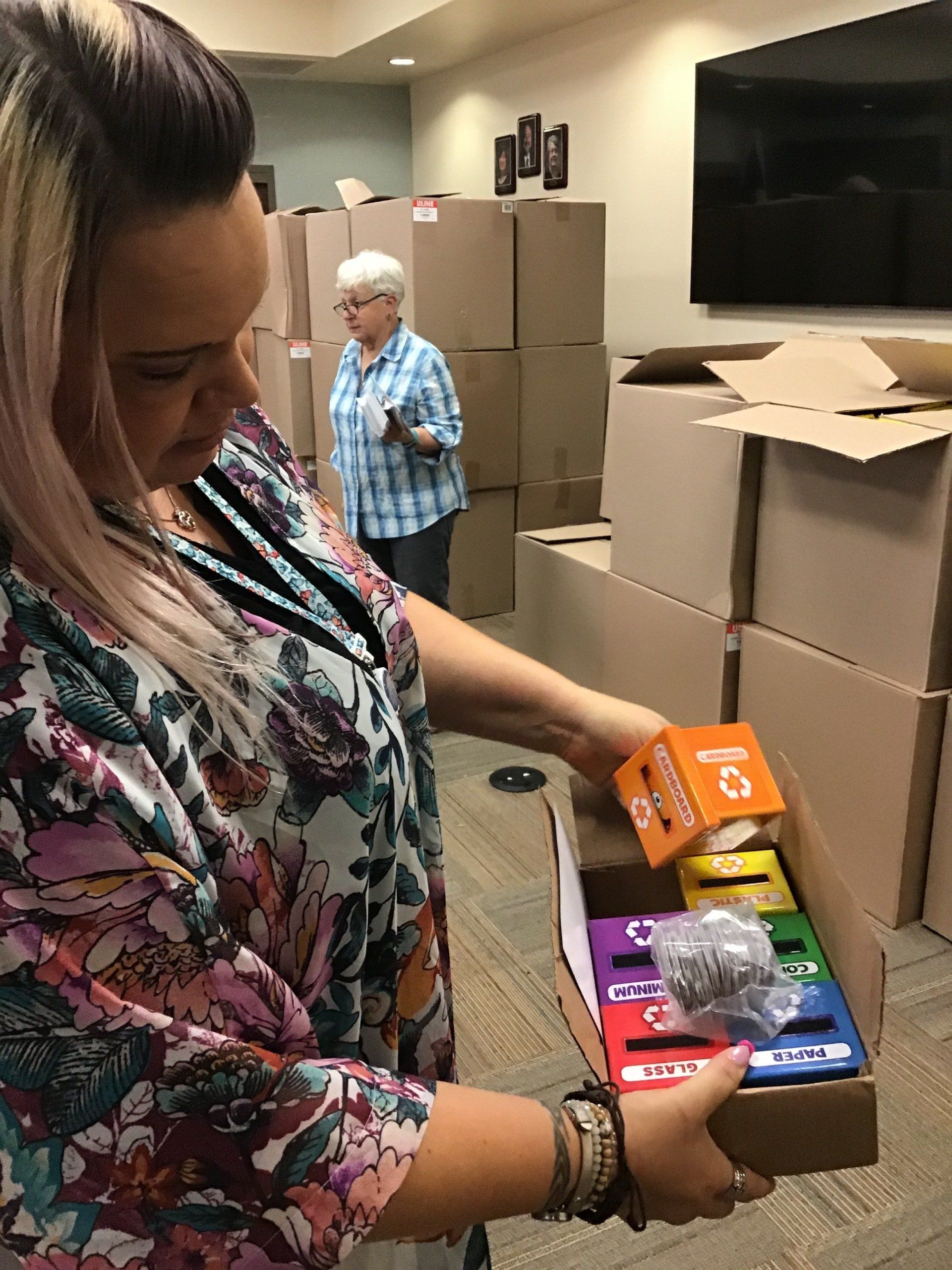 A woman is holding a box of candy in front of a stack of cardboard boxes.