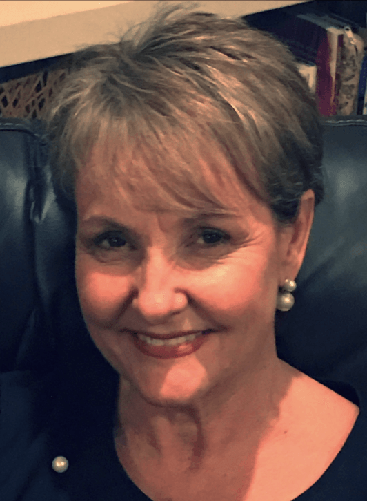 A woman wearing pearl earrings and a black shirt is smiling for the camera.