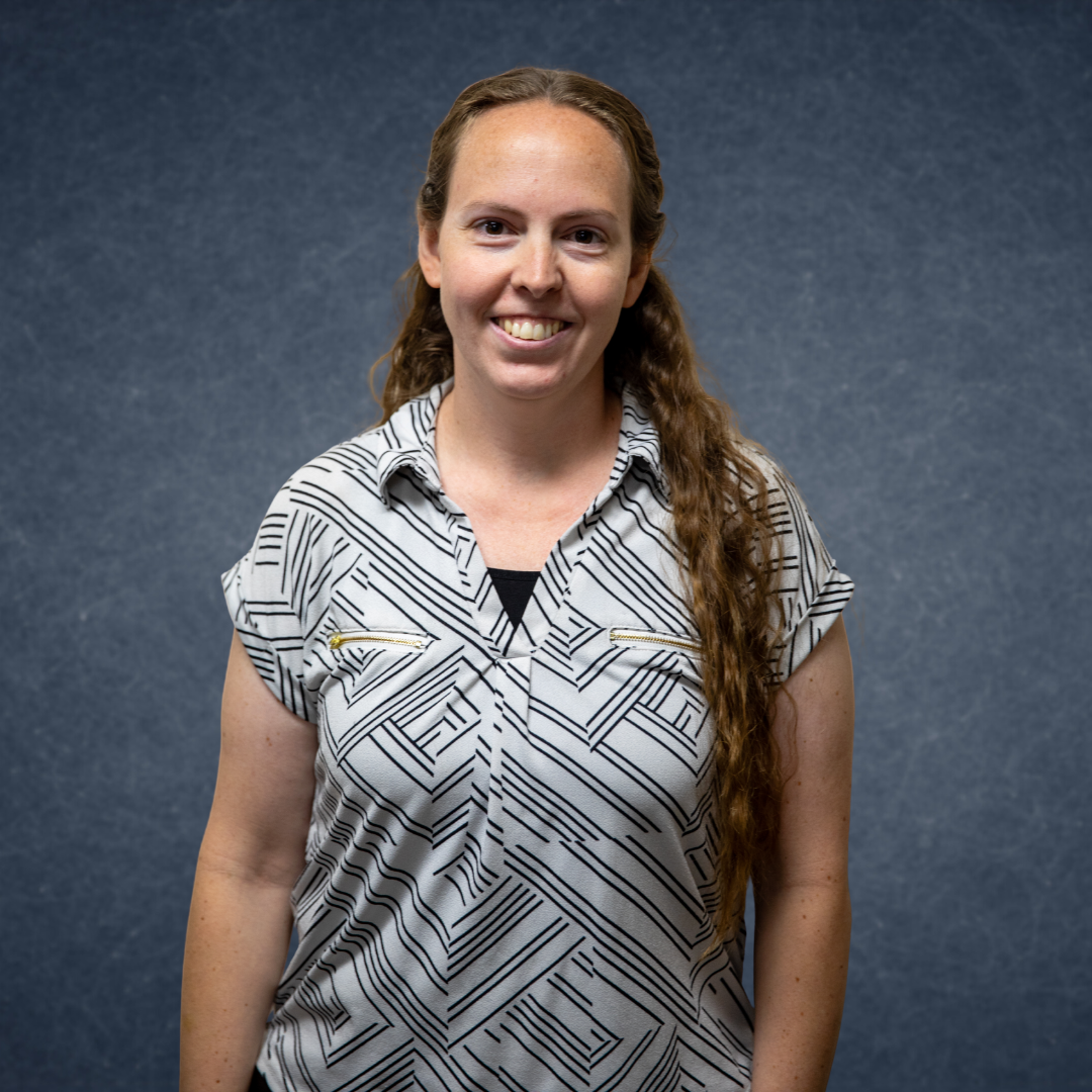 Smiling woman in a patterned blouse standing against a dark blue background