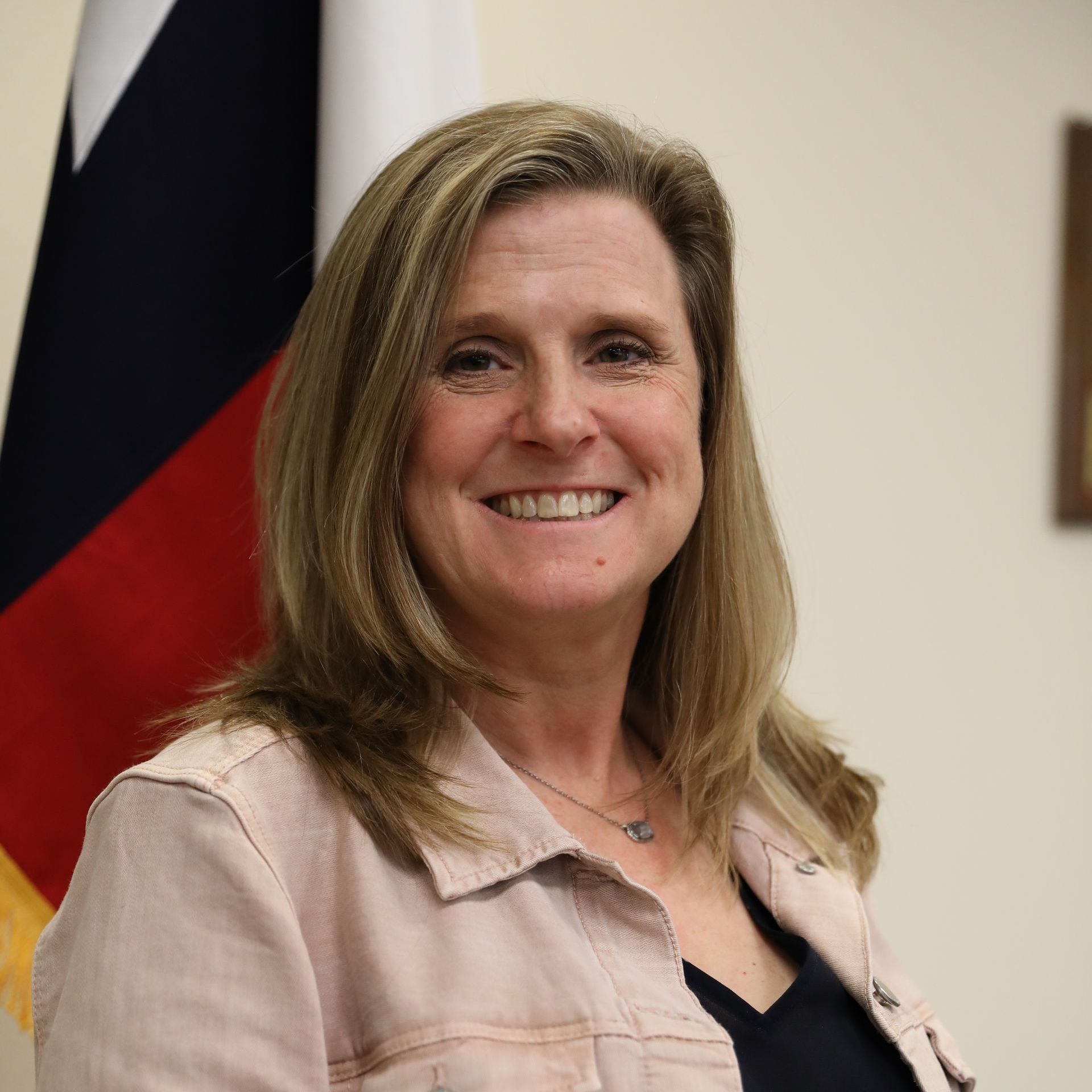 A woman in a black jacket and pearl necklace is smiling for the camera.