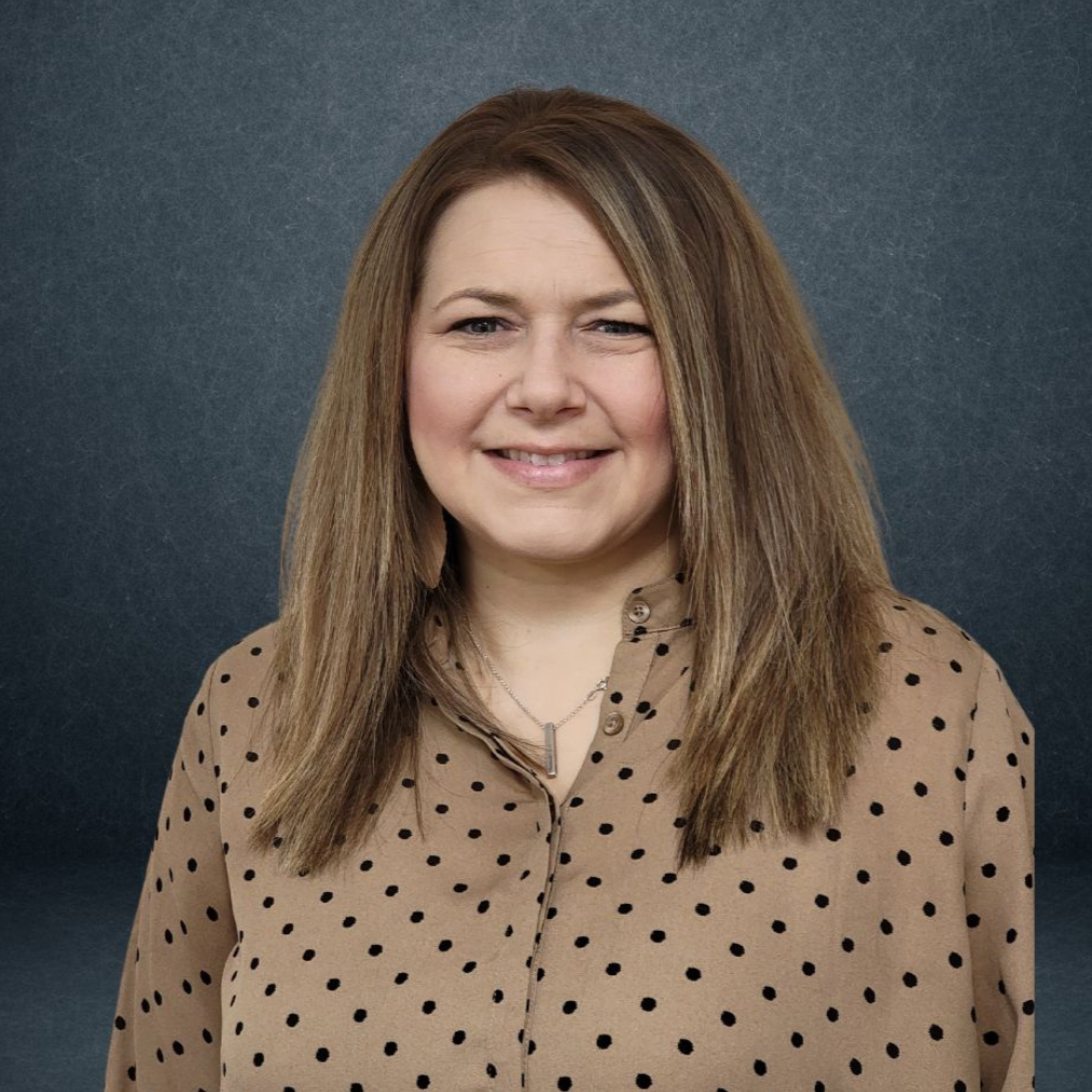 Smiling woman in a beige polka-dot blouse against a dark gray backdrop