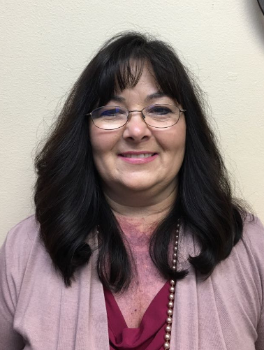 A woman wearing glasses and a pink sweater is smiling for the camera.