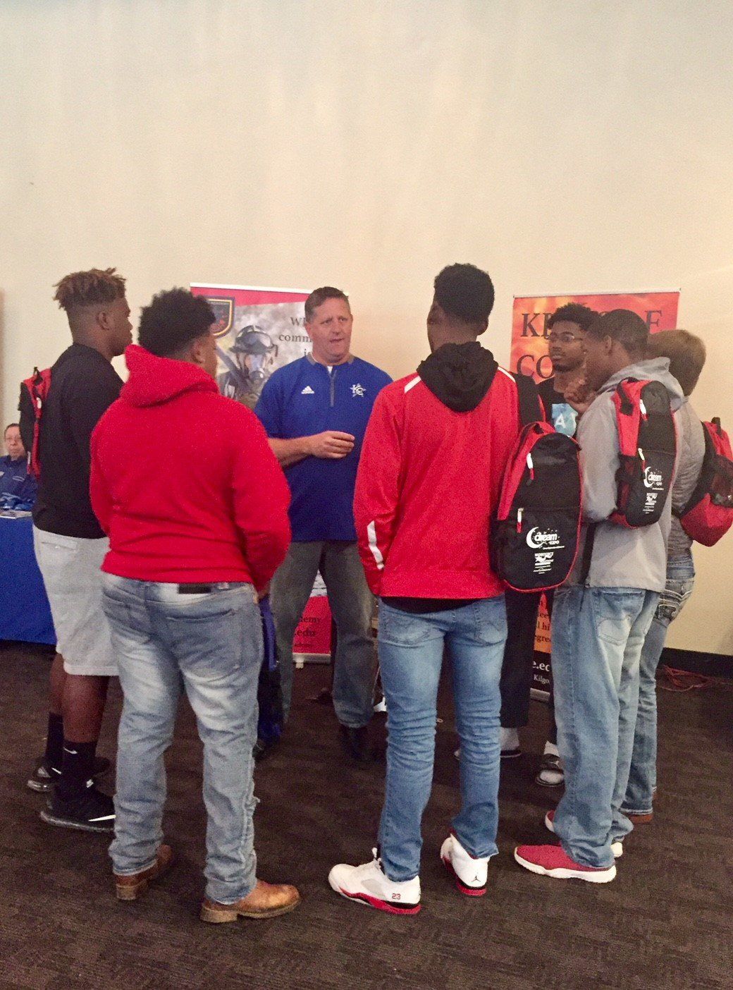 A group of young men are standing in a circle talking to a man in a blue shirt.