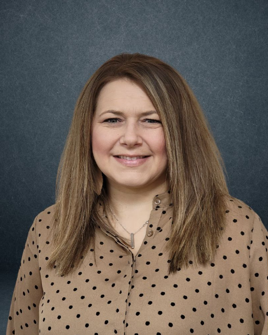 A woman wearing a polka dot shirt is smiling for the camera.