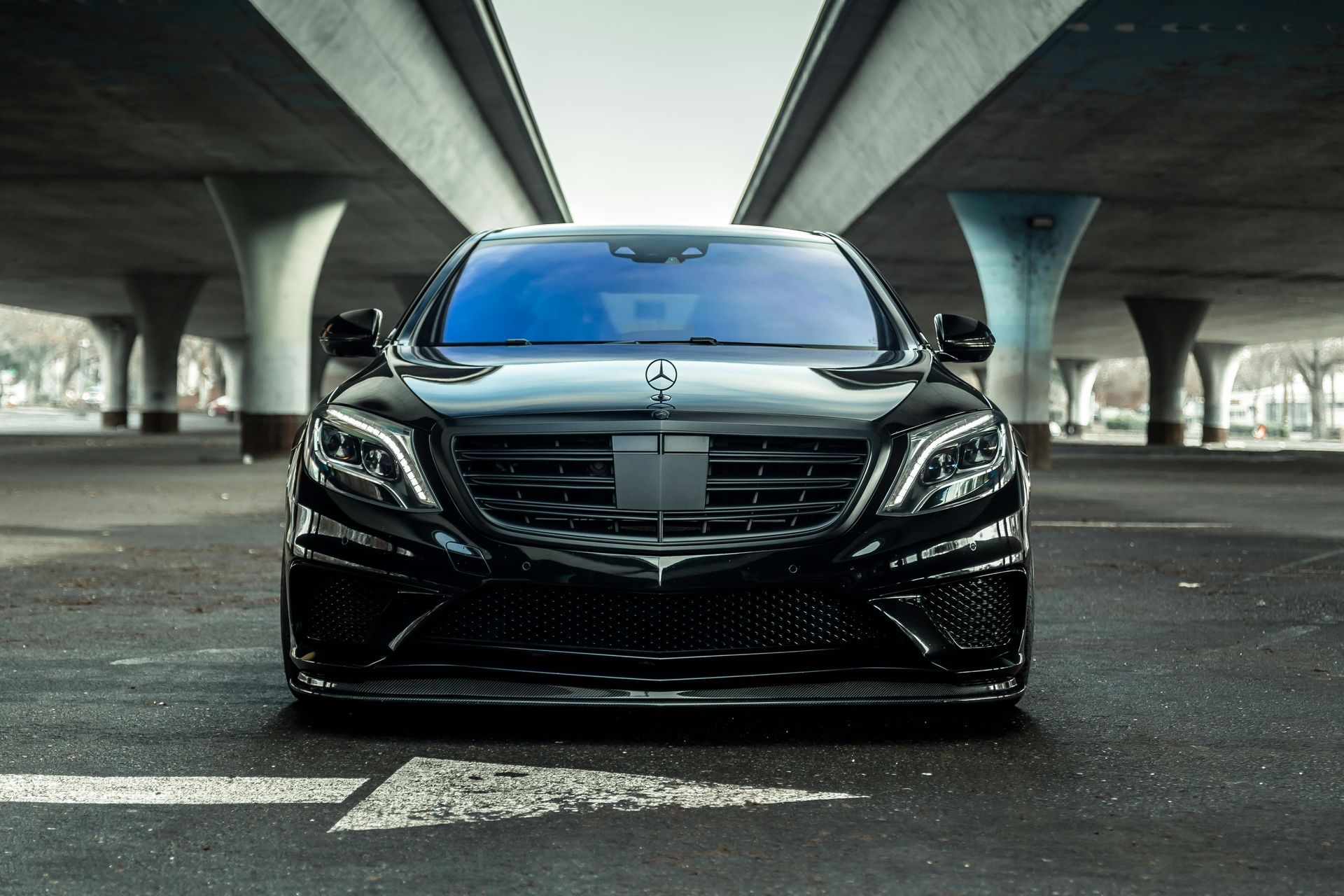 A black car is parked under a bridge in a parking lot.