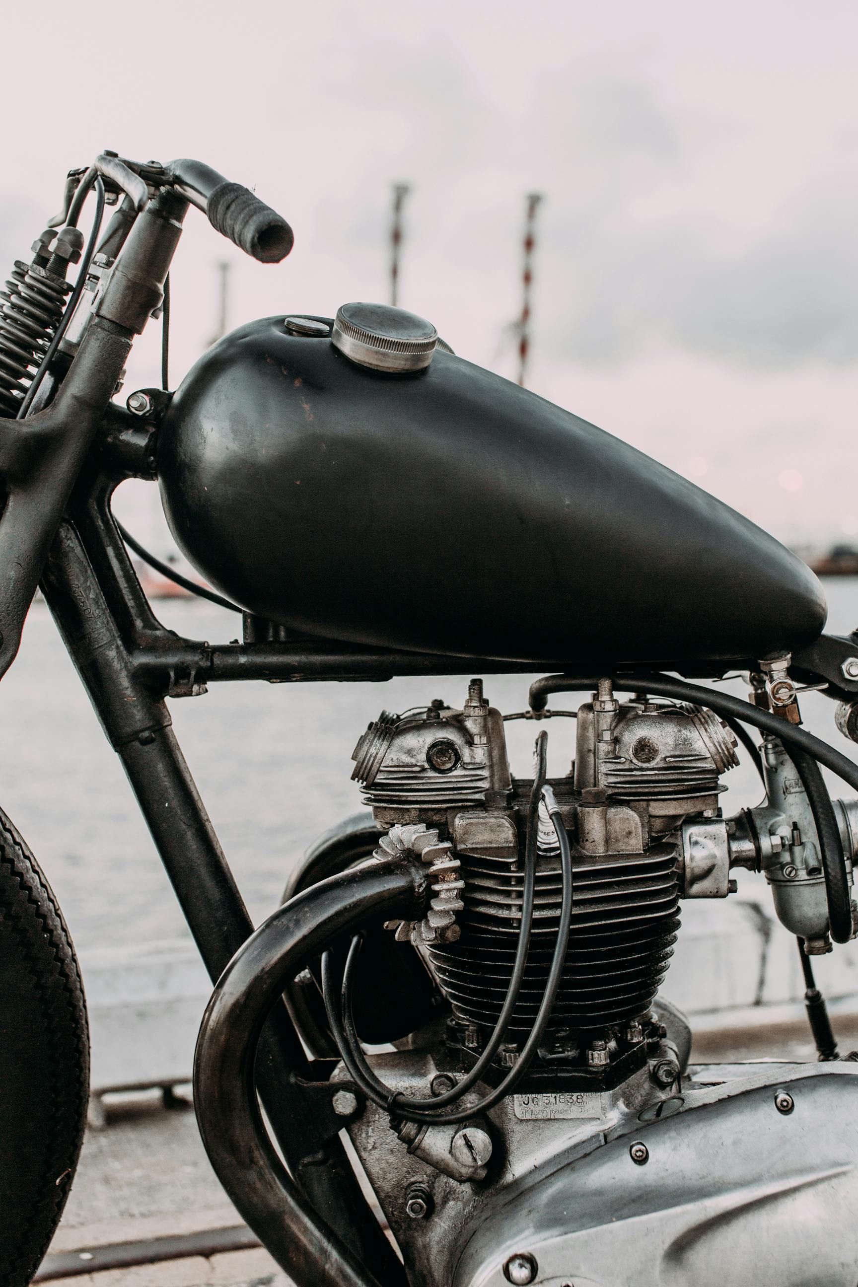 A black motorcycle with a black tank is parked next to a body of water.