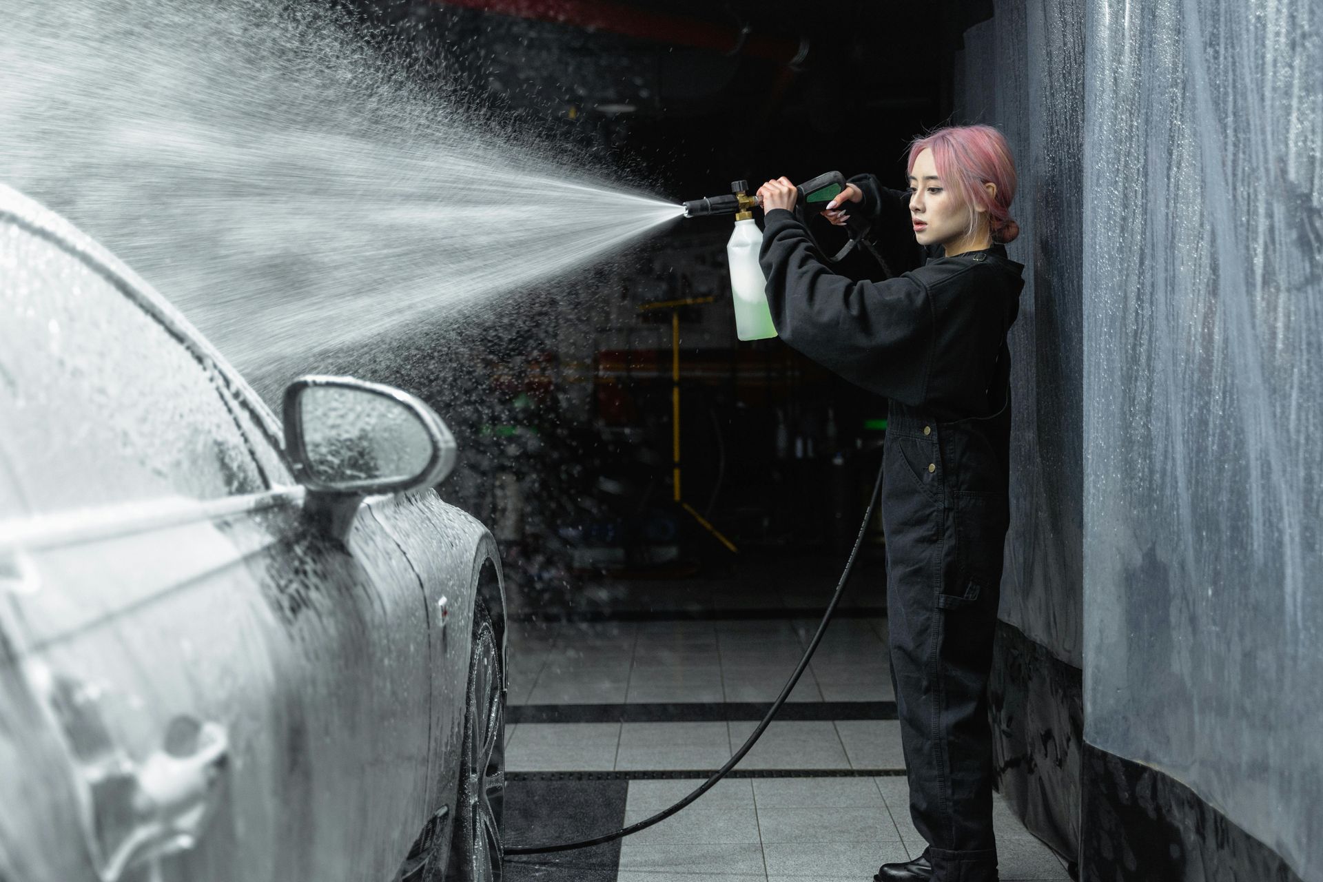 A woman is washing a car with a high pressure washer.