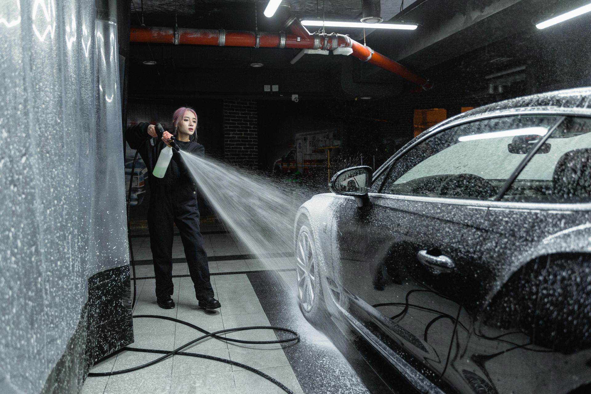 A woman is washing a car with a hose in a garage.