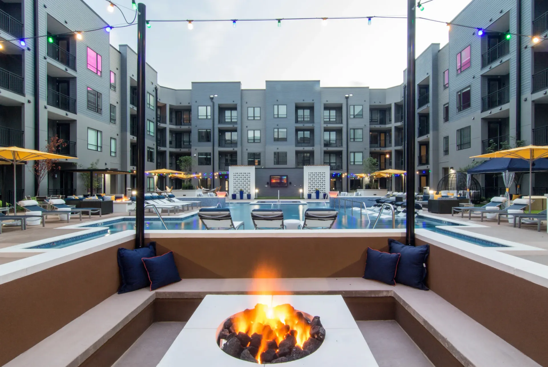 Outdoor pool courtyard with lounge seating and string lights at a modern apartment community.