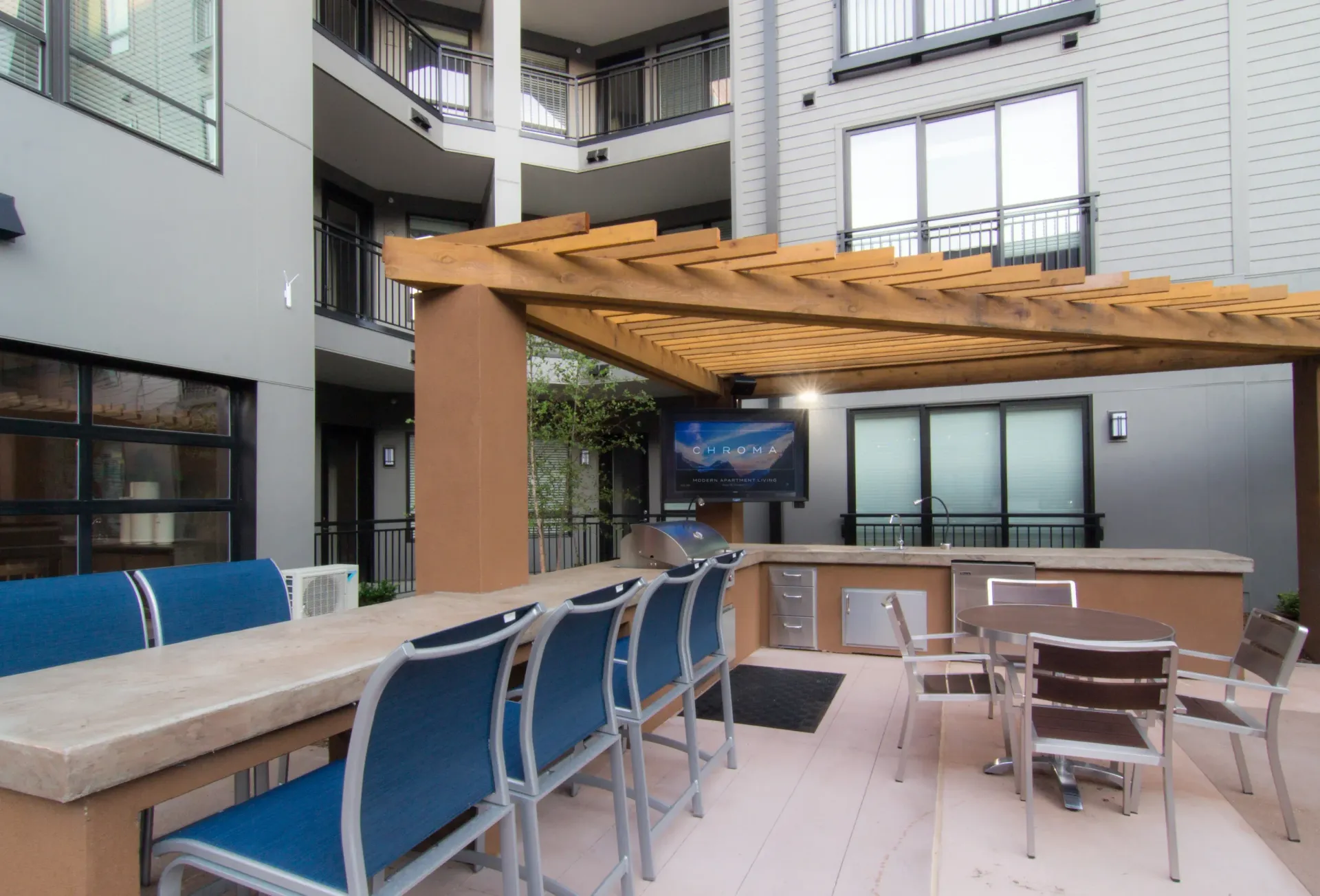 Outdoor community grilling area with seating under a wooden pergola at an apartment complex.