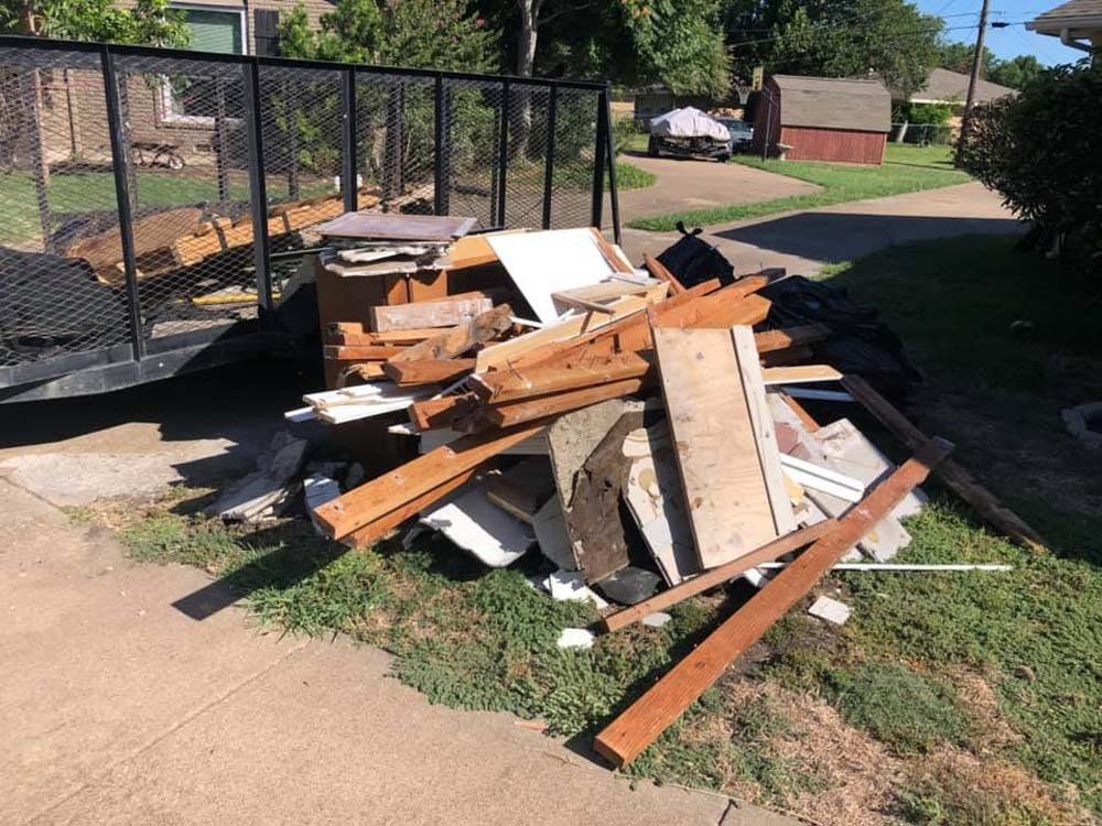 A pile of wood is sitting on the side of the road next to a trailer.