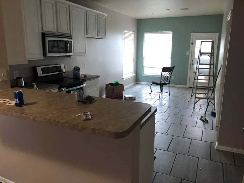 A kitchen with white cabinets , a stove , a microwave , and a chair.