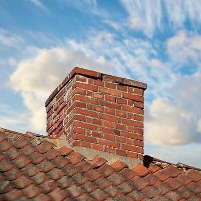 A red brick chimney sits on a tiled roof against a blue sky with soft white clouds.