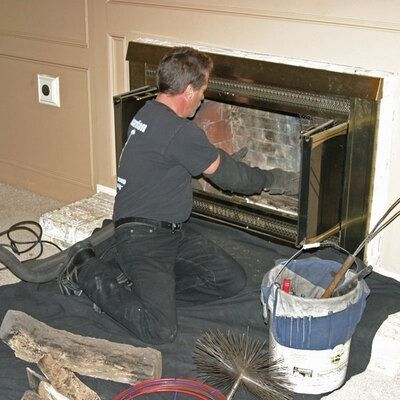 A professional cleaning a fireplace, kneeling on a protective mat with tools and a bucket nearby.