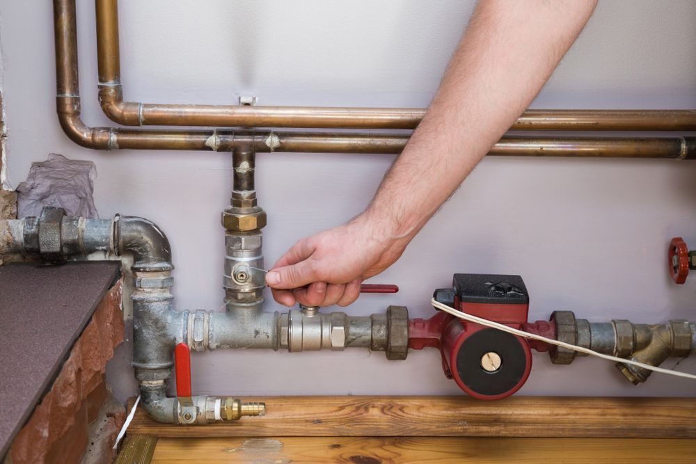 A Hand Turning A Valve On A Network Of Pipes; A Pump Is Visible
