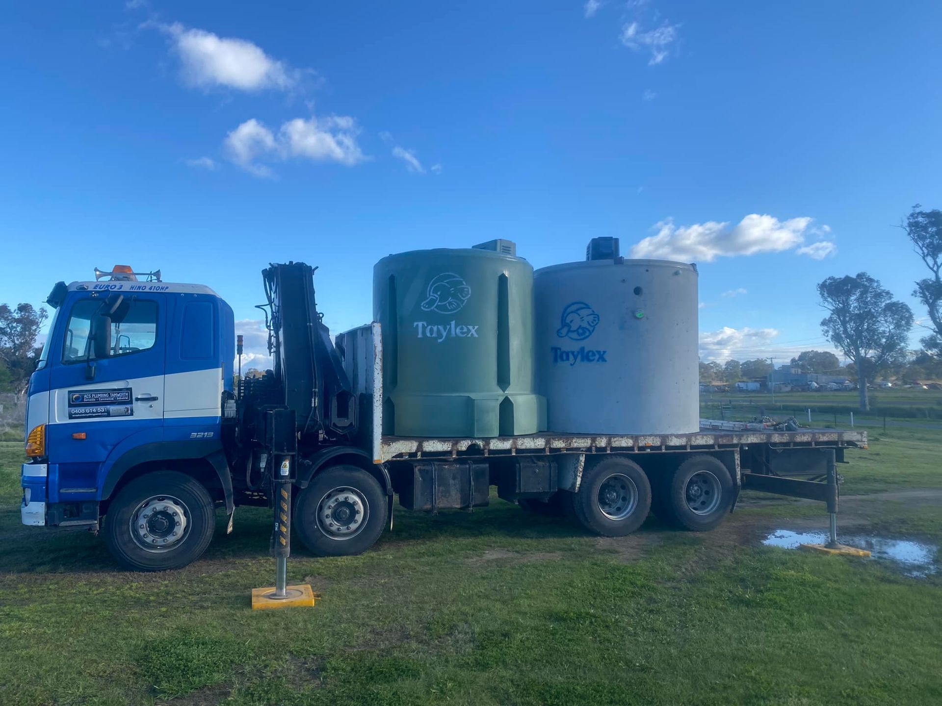 Truck Carrying Two Large Water Tanks on a Grassy Field Under a Blue Sky