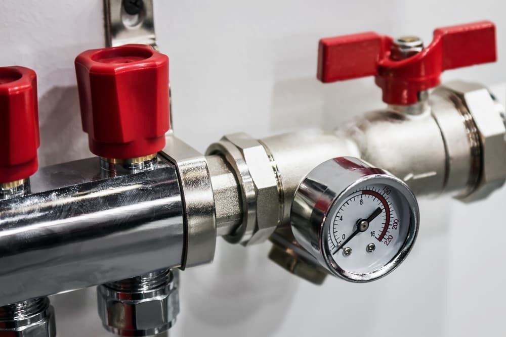 Close-up of Silver Metal Pipes With Red Valve Handles and a Pressure Gauge Against a White Wall