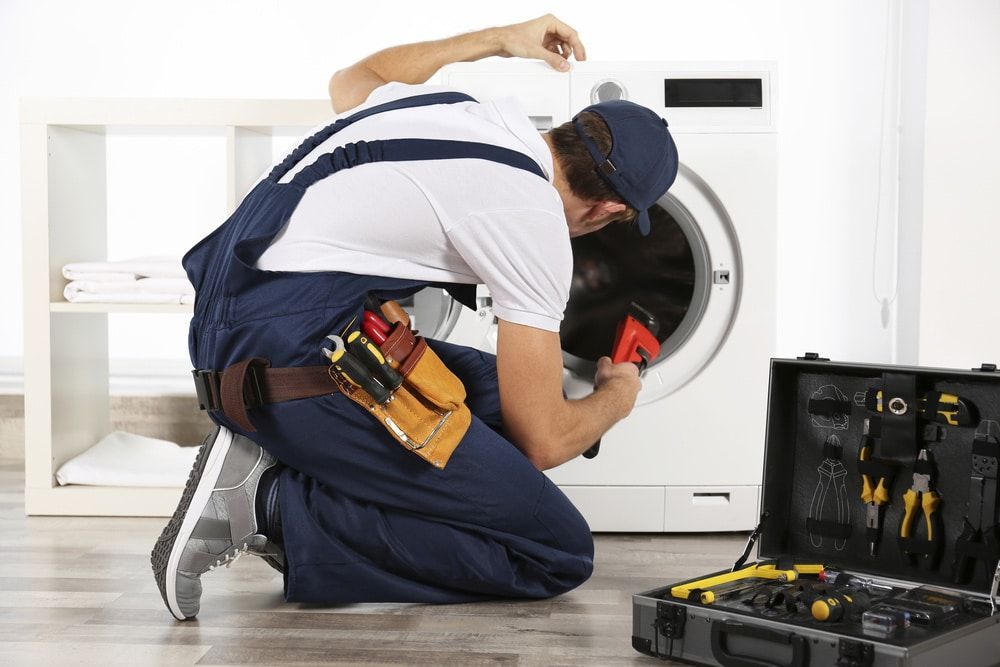 A man kneeling down working on a washing machine