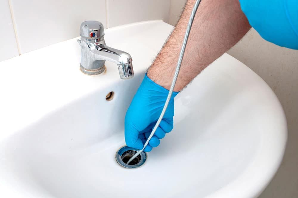 A person wearing blue gloves is cleaning a sink