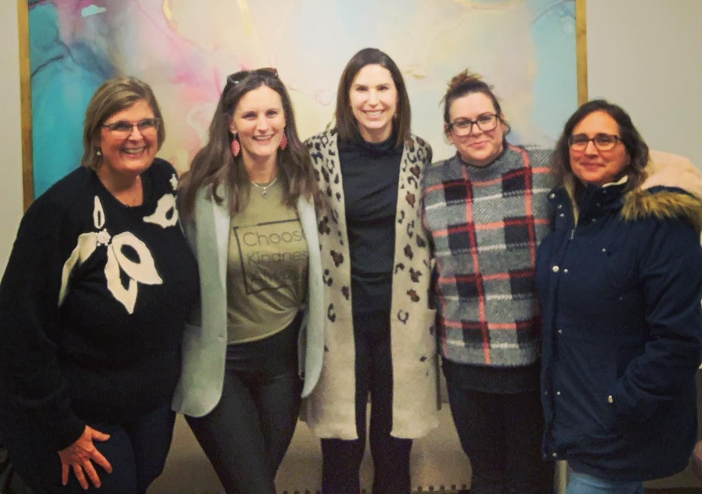Five people standing together, smiling. One wears a leopard-print coat, the others winter coats and sweaters.