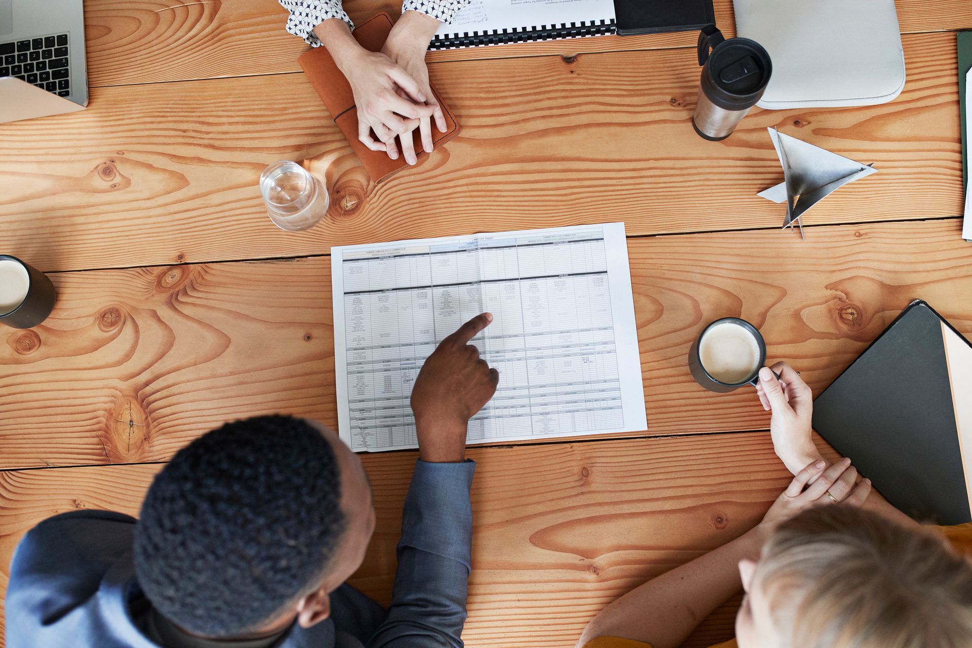 A group of people are sitting around a wooden table looking at a calendar.