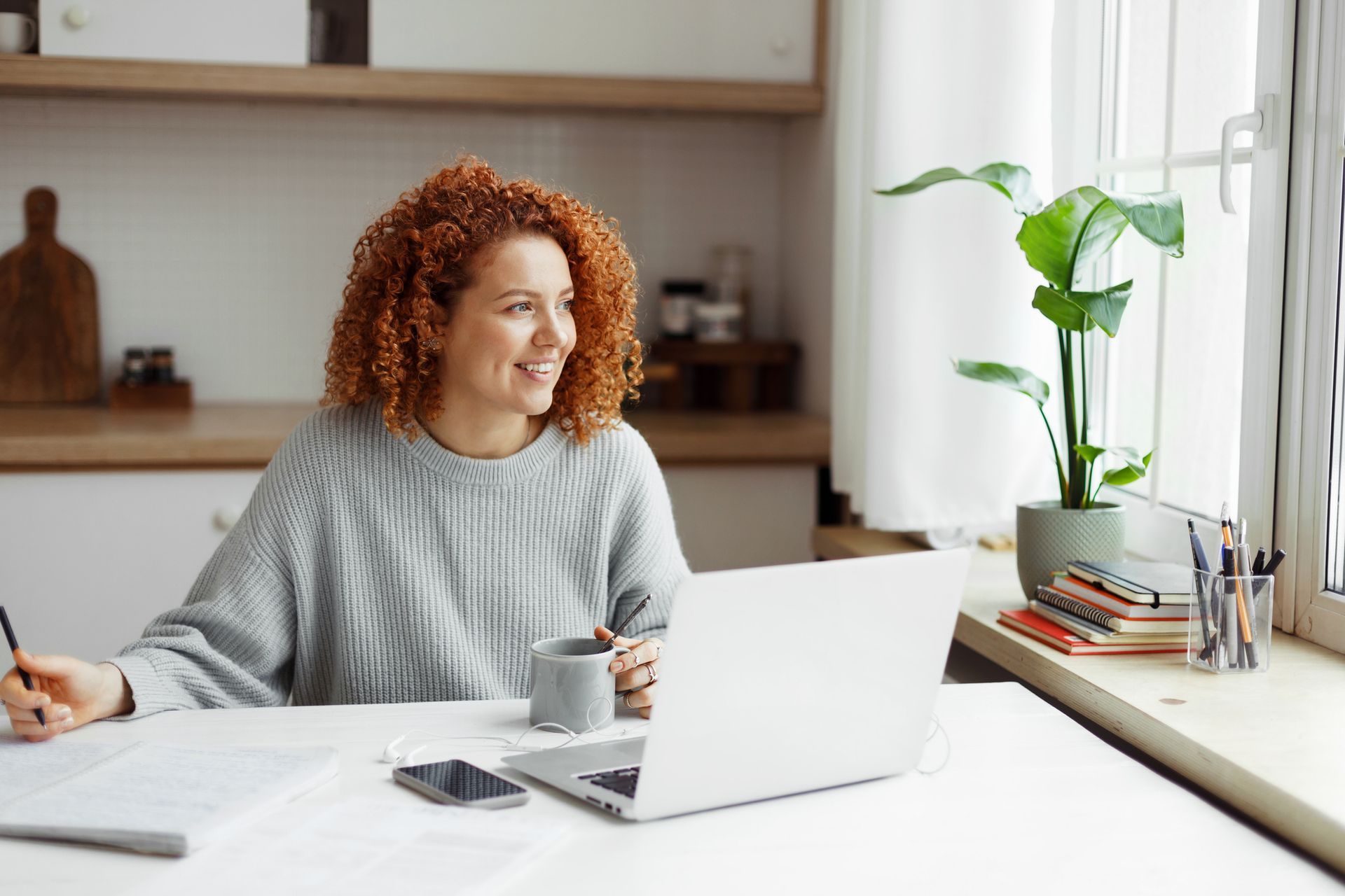 A woman is sitting at a table with a laptop and a cup of coffee.