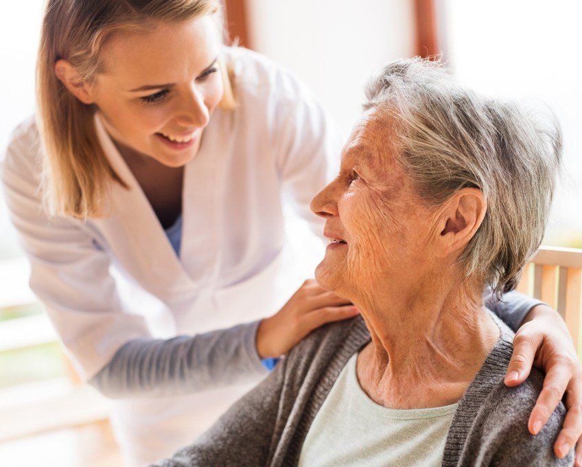 Caregiver smiling at elderly woman while holding her shoulders