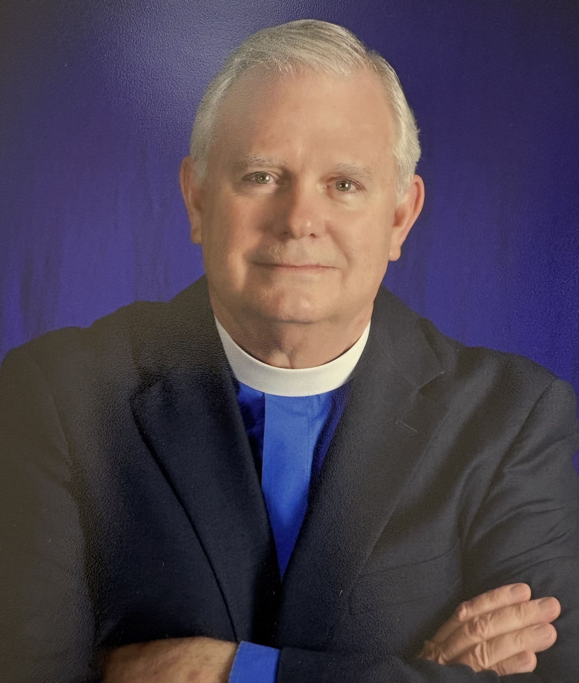 A man with white hair wearing a clerical collar. 