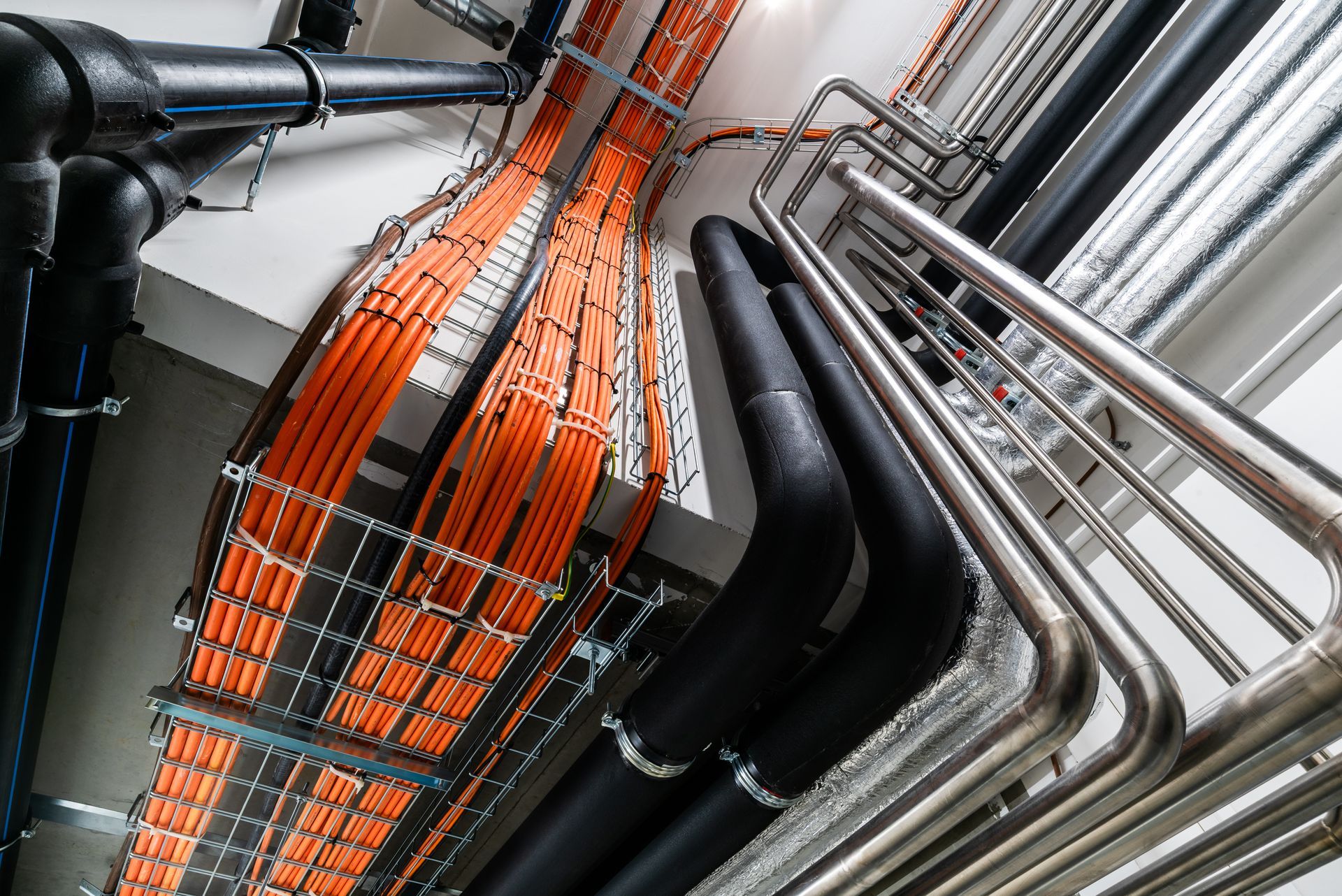 Orange and black cable tray with metal pipes and conduits in an industrial ceiling space.