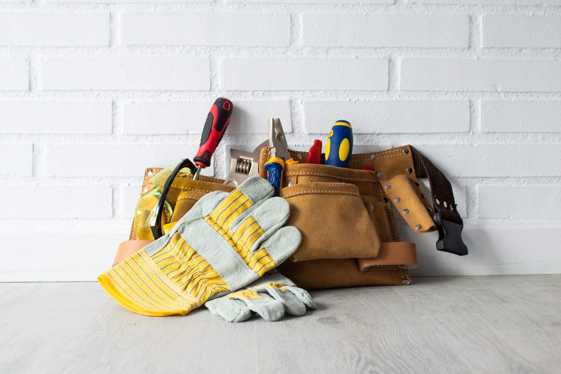 Tool belts with gloves and hand tools on a table against a white brick wall. Tool belts with gloves and hand tools on a table against a white brick wall.
