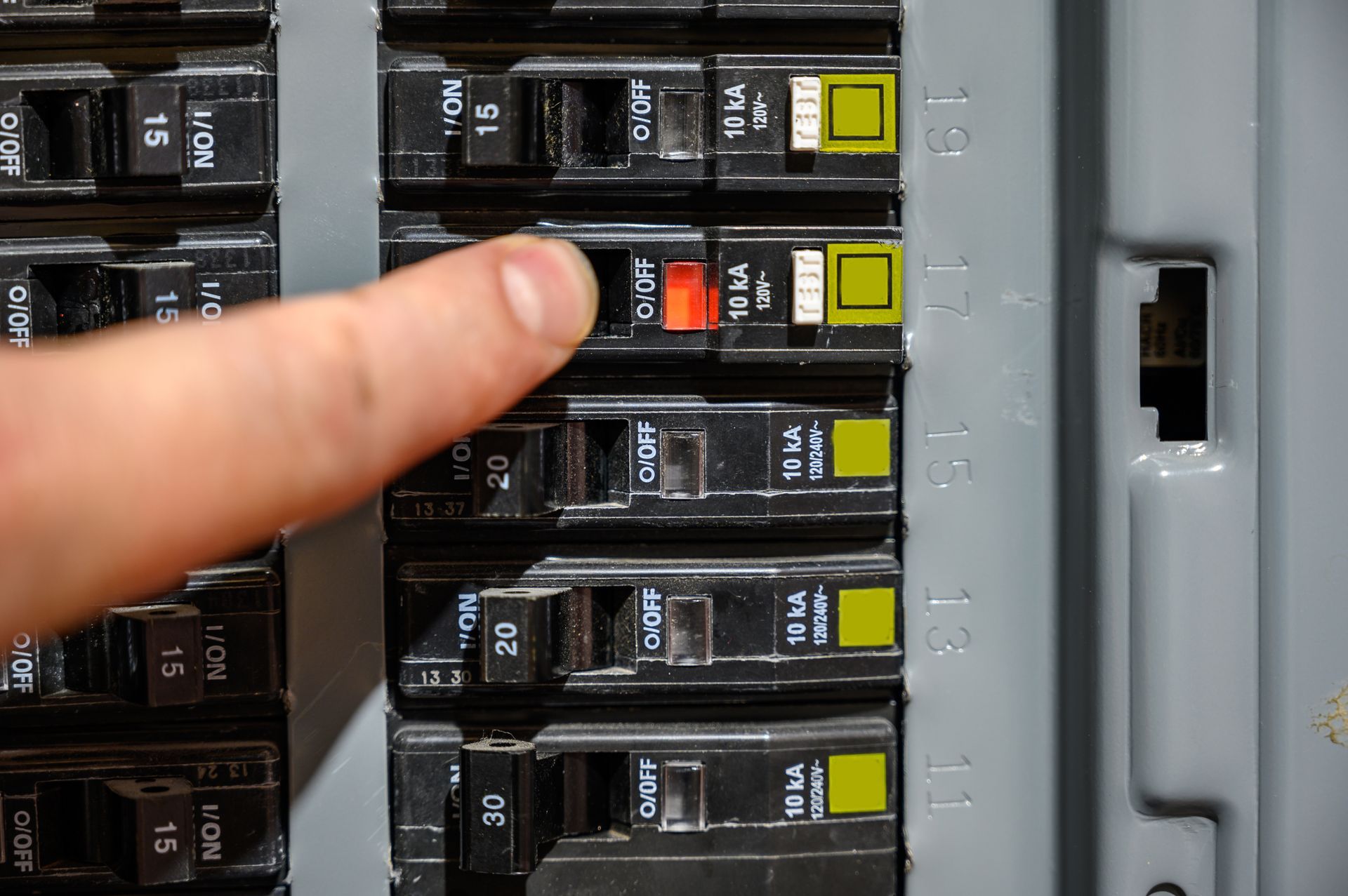 Finger pointing at a red circuit breaker in an electrical panel with yellow switches. Finger pointing at a red circuit breaker in an electrical panel with yellow switches.