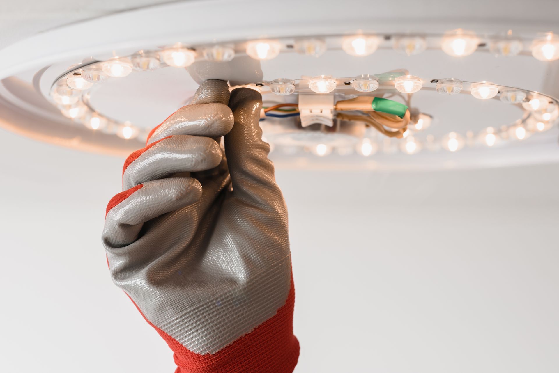 Gloved hand adjusting a ceiling light fixture with a screwdriver. Gloved hand adjusting a ceiling light fixture with a screwdriver.